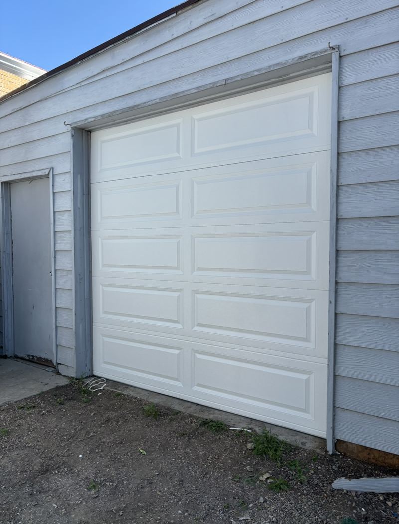 White raised-panel single-car garage door on a gray-sided garage
