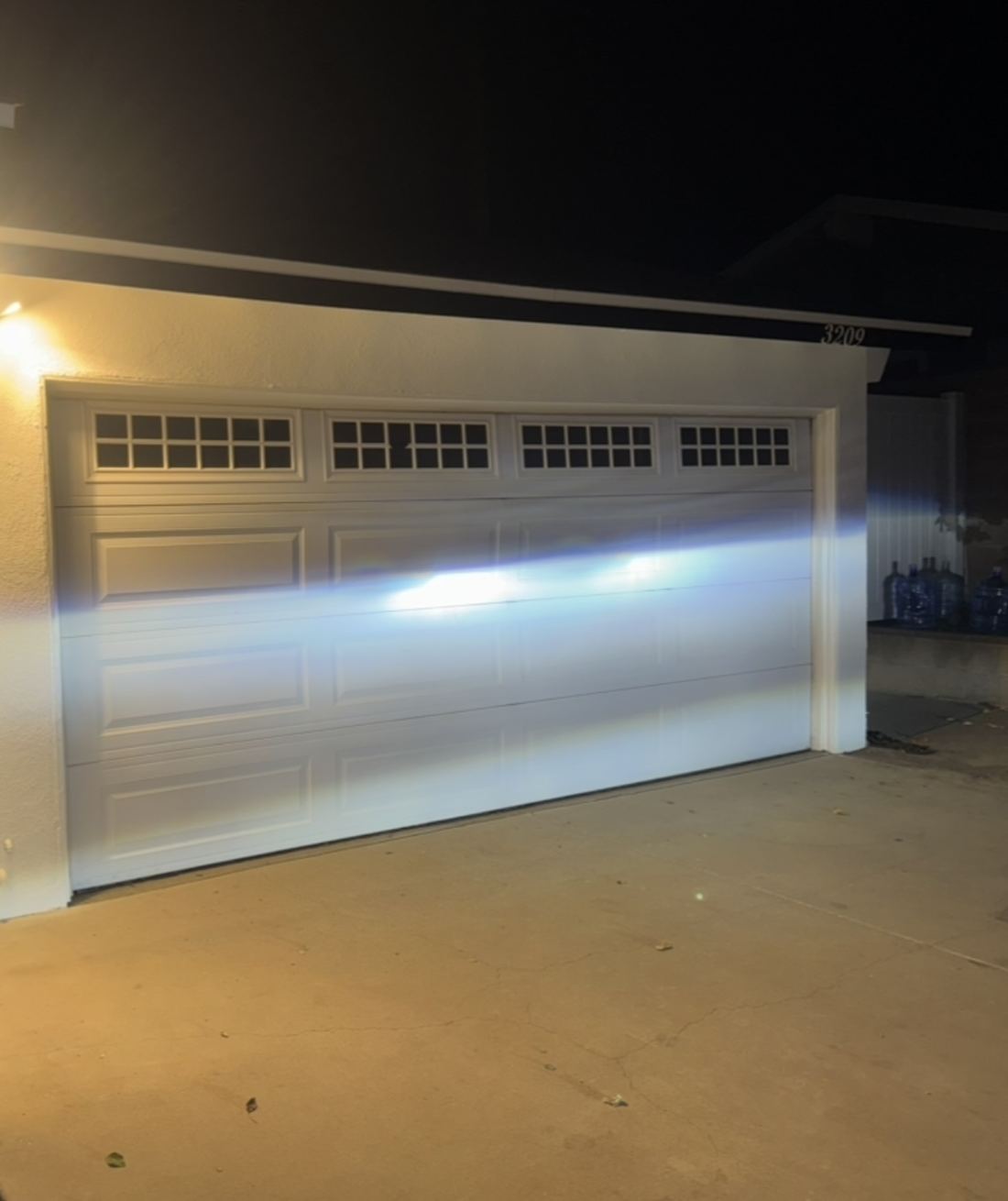 Finished white raised-panel double garage door with a row of windows, lit at night